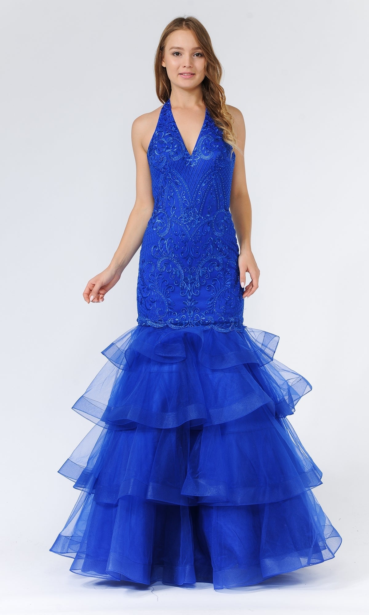 A woman models the Beaded Long Halter Mermaid Tiered Prom Dress 8466 in bright blue, featuring intricate embroidery, beaded details, and a layered tulle skirt, against a plain white background.